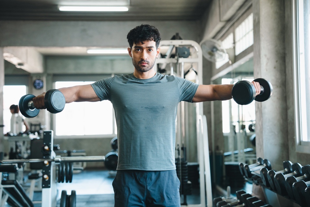 Man doing dumbbell lateral raises in a gym, an exercise that can lead to shoulder injury, shoulder impingement and shoulder tendinopathy without the right shoulder physiotherapy advice
